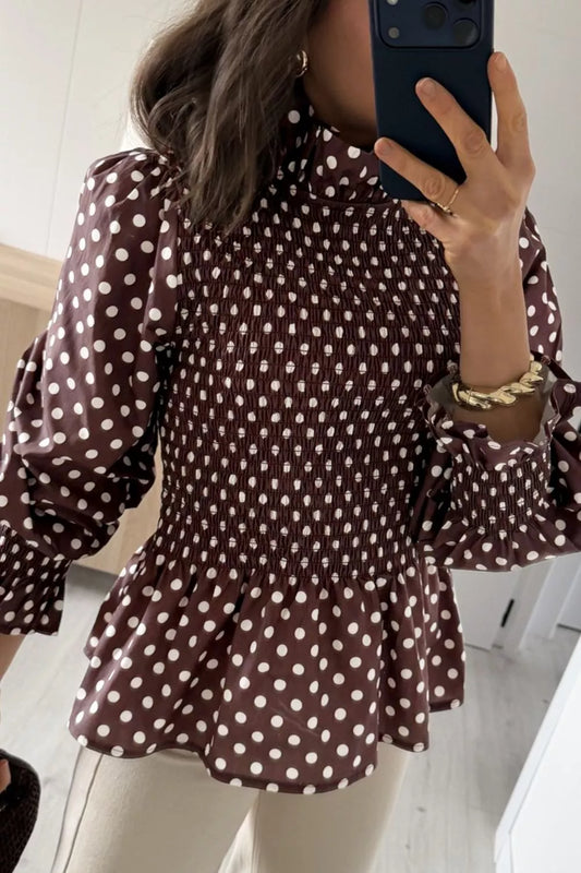 Vista frontal de blusa marrón con lunares blancos, cuello alto, cintura fruncida y mangas abullonadas con puños de volantes. NINA AURA COLLECTION.