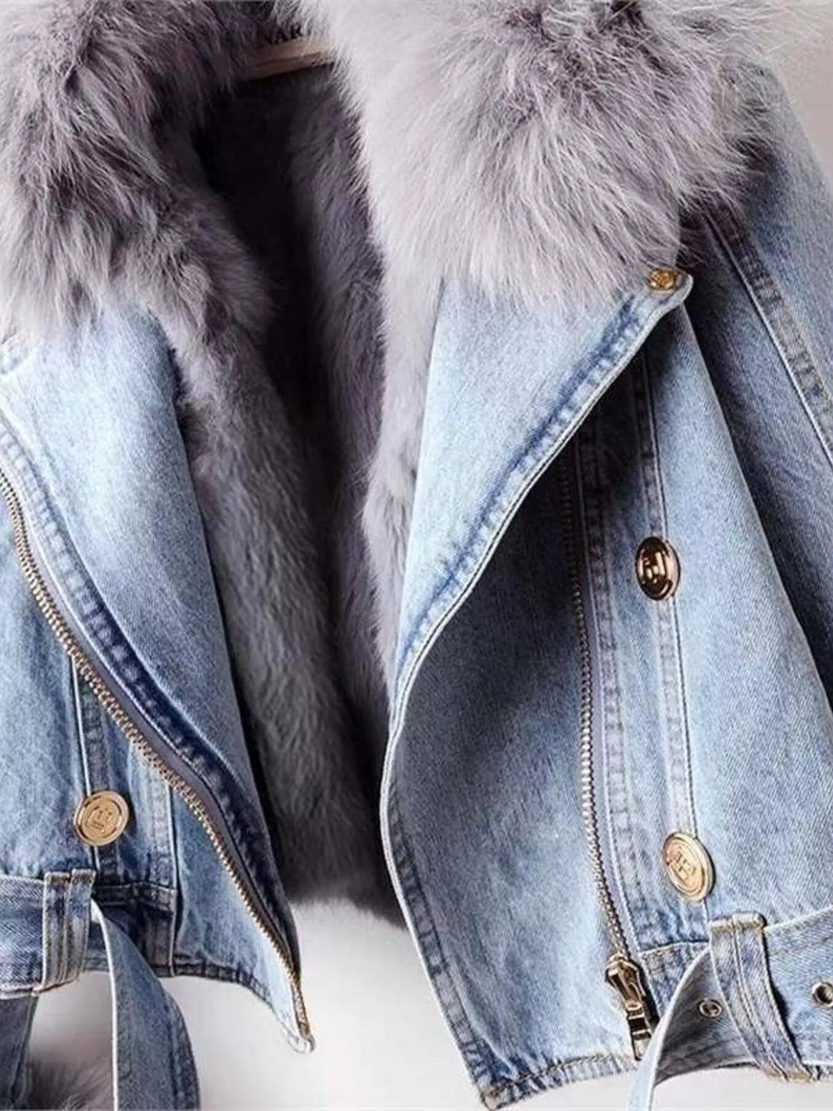 Detalle de chaqueta vaquera azul claro con cuello de pelo sintético gris, cierre de cremallera diagonal y botones metálicos dorados.
