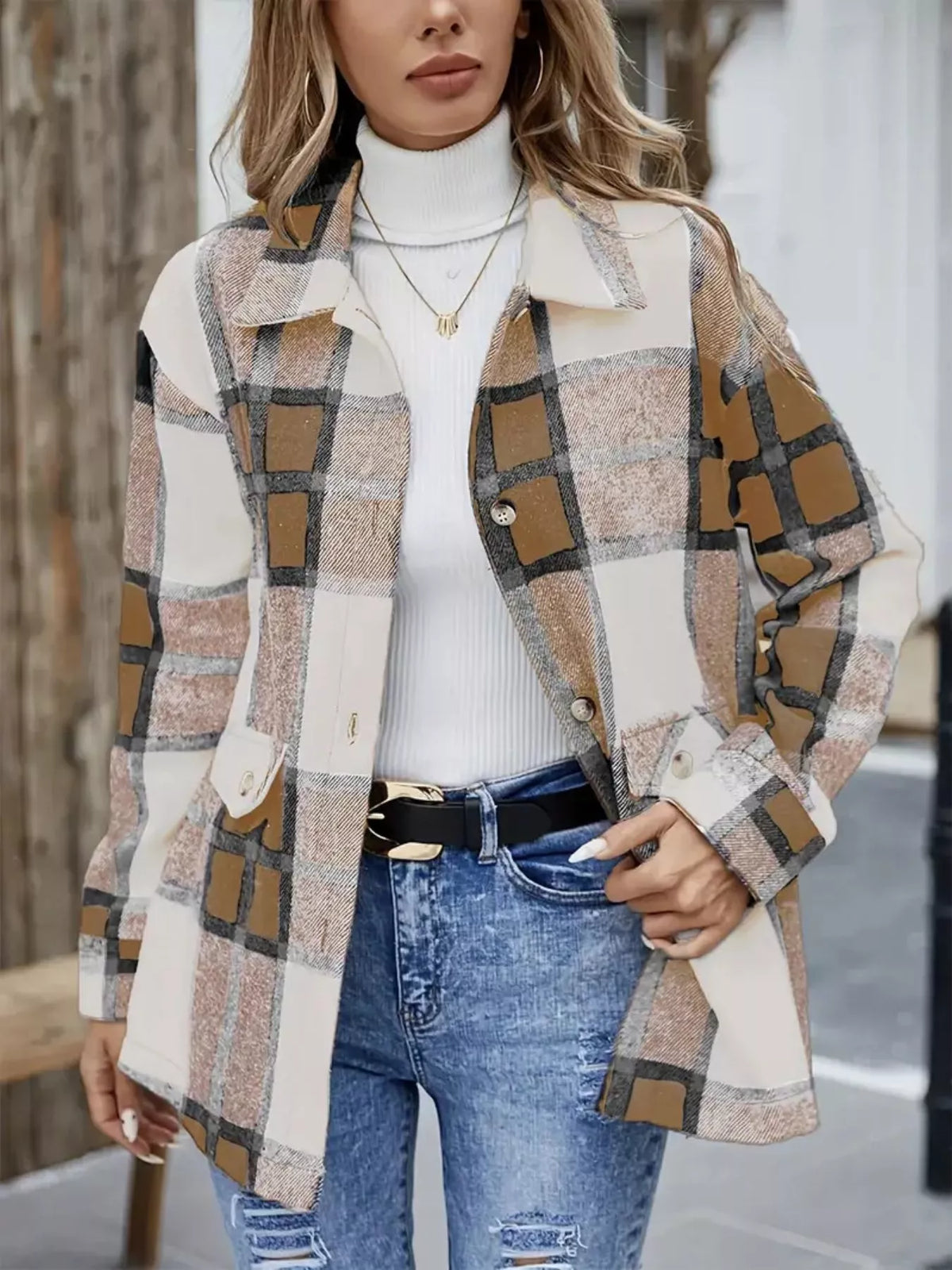 Mujer con sobrecamisa larga de cuadros camel, beige, blanco y gris, cuello camisero, botones delanteros y bolsillos, combinada con jersey blanco y vaqueros.